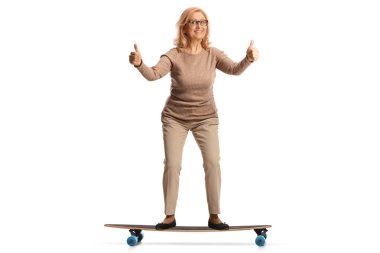 Middle aged woman riding a skateboard and gesturing thumbs up isolated on white background