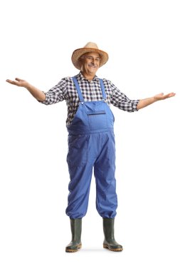 Mavi tulumlu olgun bir çiftçinin tam boy portresi beyaz arka planda izole edilmiş hoş geldin işareti yapıyor.
