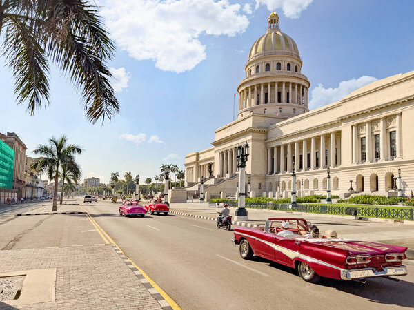 Convertible cars driving on the street in front of El Capitolio building in Cuba, Havana
