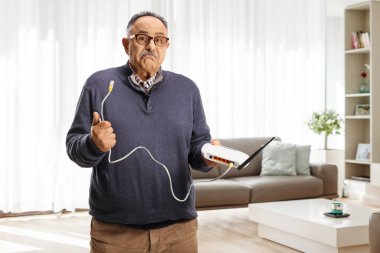 Oturma odasında modem kablosu tutan kafası karışmış olgun bir adam.