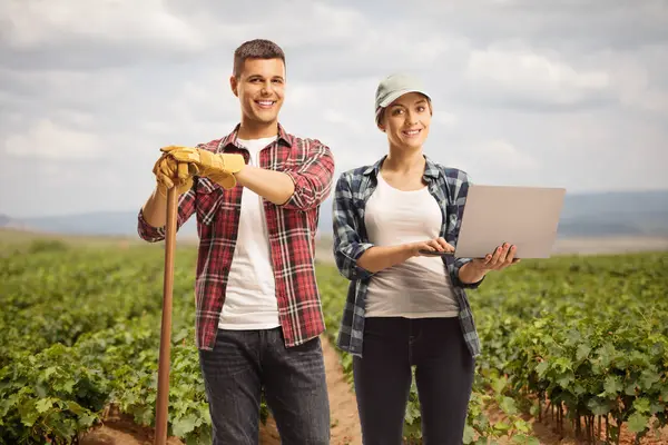 Male and female farmers with a laptop computer standing on a vineyard