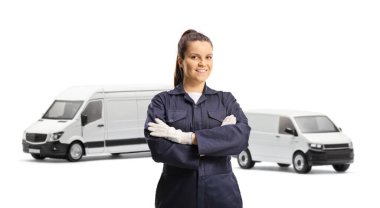 Üniformalı ve eldivenli genç bayan tamirci beyaz arka planda izole edilmiş minibüslerin önünde poz veriyor.