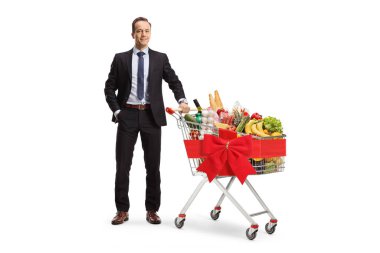 Beyaz arka planda kırmızı kurdeleyle bağlanmış alışveriş arabasıyla poz veren bir işadamı.