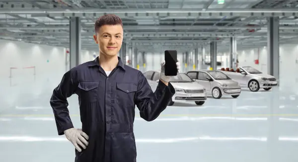 Young mechanic holding a mobile phone inside a garage with vehicles