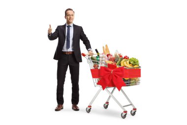 Bir iş adamının tam boy portresi, beyaz arka planda izole edilmiş gıda hayır kurumu konsepti, alışveriş arabasında yiyecekler ile başparmağını kaldırıyor.