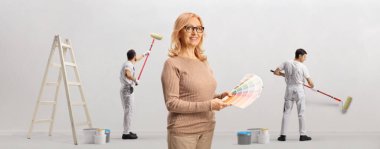 Renk paleti tutan kadın ve ressam arkada bir duvar boyuyor.