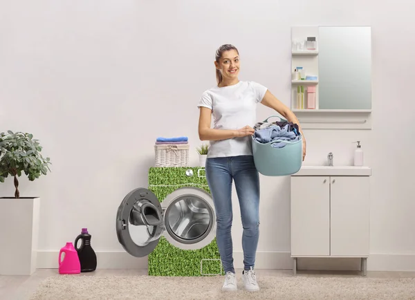 Woman in a bathroom with a power efficient washing machine holding a laundry basket and smiling