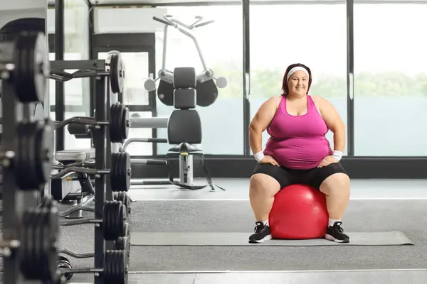 肥胖的女人坐在体育馆的健身球上 对着镜头笑 — 图库照片