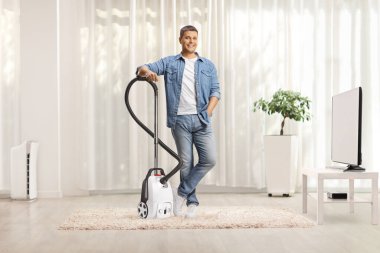 Evdeki elektrikli süpürgeye gülümseyen ve yaslanan bir adam.