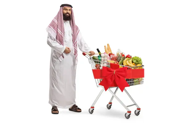 沙乌地阿拉伯男子站在购物车旁 购物车里装满了食品和红色缎带 与白色背景隔离在一起 — 图库照片