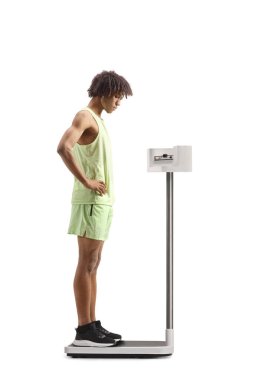 Beyaz arka planda izole edilmiş tıbbi bir ölçekte ağırlığı kontrol eden spor giysili Afrikalı Amerikalı bir adam.