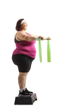 Ayrıca beyaz arka planda elastik bantla egzersiz yapan boyda bir kadın.