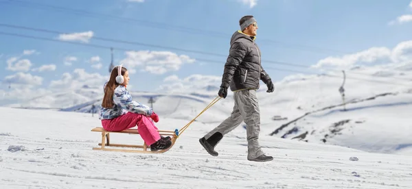 Kışlık Elbiseli Bir Adam Dağ Tepesinde Kızaklı Bir Kızı Çekiyor — Stok fotoğraf