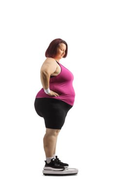 Spor giyim sektöründe şişman bir kadın ağırlığını beyaz arka planda izole edilmiş bir ölçekte kontrol ediyor.