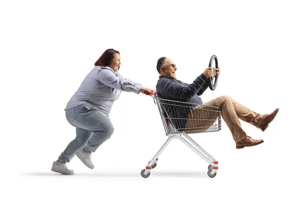 一个女人把一个带着方向盘的成熟男人推进一辆白色背景的购物车 — 图库照片
