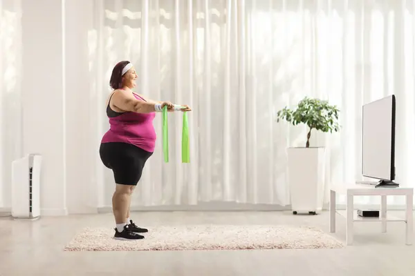 Woman exercising with elastic band and watching aerobic class on tv at home