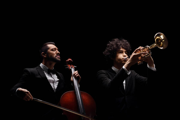 Male musicians playing a cello and a trumpet isolated on black background