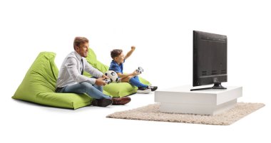 Baba ve oğul evde joystick ile futbol oynuyorlar.