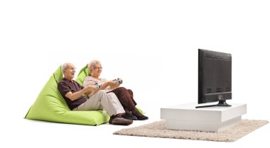 Televizyon oyunu oynayan yaşlı bir çift ve beyaz arka planda izole edilmiş puf minderlerin üzerinde oturuyor.