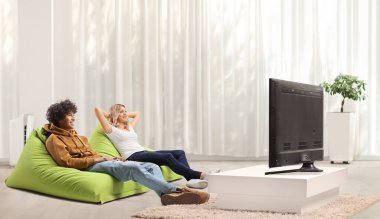 Genç bir adam ve bir kadın bir salonda televizyon karşısında dinleniyorlar.