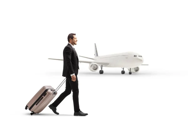 白い背景に隔離された飛行機の近くでビジネスマンの散歩とスーツケースを引っ張る完全な長さのプロフィールショット — ストック写真