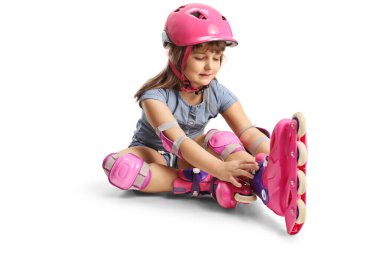 Yerde oturan ve beyaz arka planda izole edilmiş paten giyen bir kız.