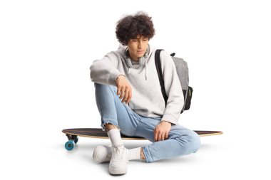 Beyaz arka planda izole edilmiş kaykayın üzerinde oturan düşünceli genç adam.