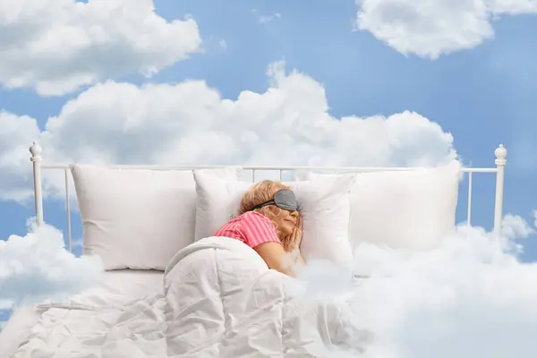 Woman sleeping with a mask and floating on clouds in the sky