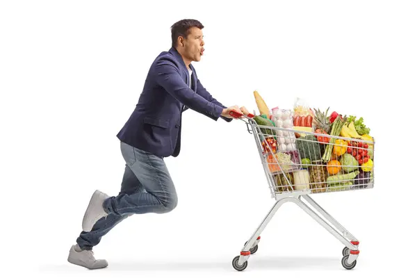 白い背景に隔離されたスーパーマーケットのショッピングカートで走っている興奮する男のフル長さのプロフィールショット — ストック写真