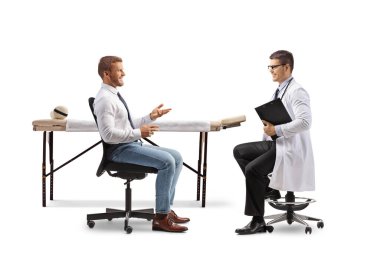 Beyaz arka planda izole edilmiş bir sandalyede oturan bir erkek doktorla konuşan bir iş adamının tam boy profil çekimi.