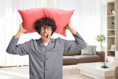 Pijamalı kızgın genç adam kafasında yastıkla evde bağırıyor.