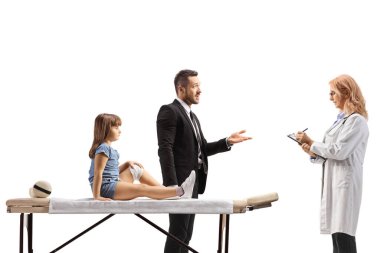 Dizinden yaralanmış bir çocuk fizik tedavi yatağında oturuyor ve babası beyaz arka planda izole edilmiş bir doktorla konuşuyor.