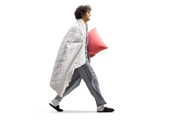 穿着睡衣 裹着毛毯 背着枕头 独立行走在白色背景下的年轻人 — 图库照片