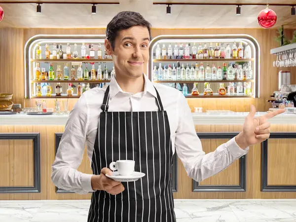 stock image Waiter holding an espresso coffee and pointing at a bar