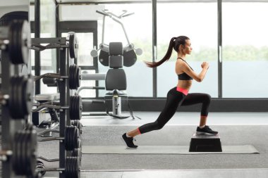 Genç bir bayanın spor salonunda spor yaparken tam boy profil çekimi.