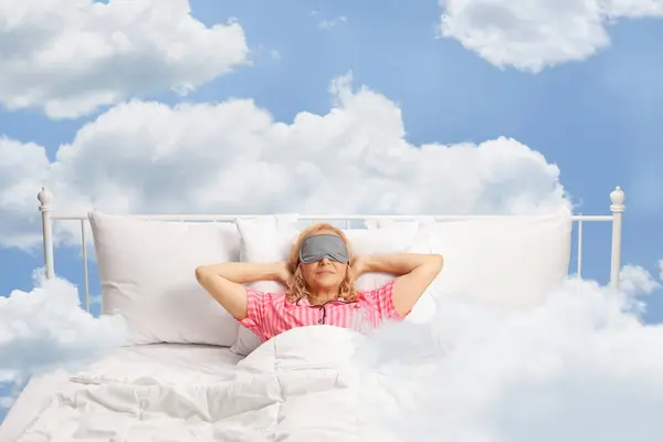 Woman up in the clouds resting in a bed with mask over eyes