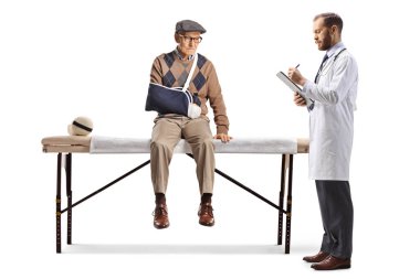 Kırık kollu yaralı yaşlı bir adam beyaz arka planda izole edilmiş bir doktorla tıp yatağında oturuyor.