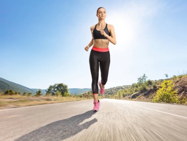 Güneşli bir günde asfalt yolda koşan sağlıklı genç bir kadın.