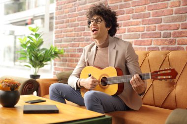 Kanepede oturup gitar çalan mutlu genç bir adam.