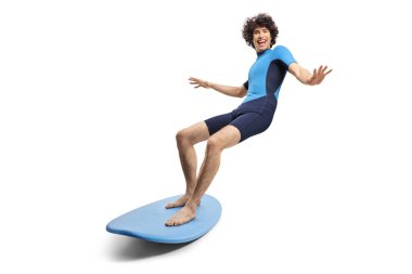 Dalış kıyafetli genç adam beyaz arka planda izole bir sörf tahtası kullanıyor.