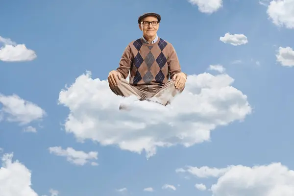 ヨガで雲の上に座っている高齢男性が空に現れる ロイヤリティフリーのストック写真