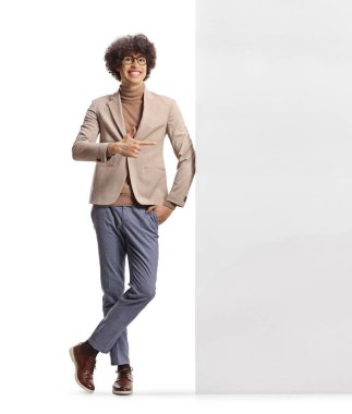 Uzun boylu, kıvırcık saçlı, duvara yaslanmış ve beyaz arka planda izole edilmiş birini işaret ediyor.