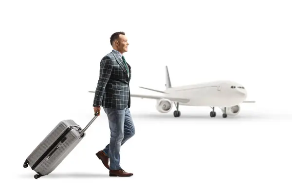 スーツとジーンズの男の完全な長さのプロフィールショットと白い背景に隔離された空港でスーツケースを引っ張る ストックフォト
