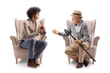 Kıvırcık saçlı ve gözlüklü genç adam bir koltukta oturuyor ve beyaz arka planda izole edilmiş yaşlı bir adamı dinliyor.