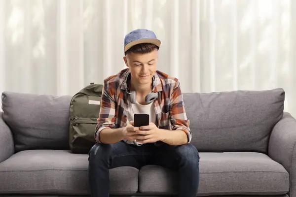 Laki Laki Remaja Duduk Sofa Dengan Headphone Dan Menggunakan Smartphone Stok Gambar