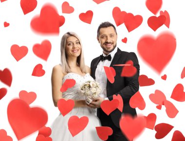Mutlu bir evliliği olan gelin ve damat, beyaz arka planda kırmızı kalplerin altında dikiliyor.