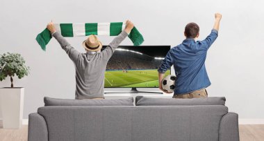 Genç ve yaşlı bir adamın TV 'de futbol maçı izlemesi ve evde tezahürat yapması.