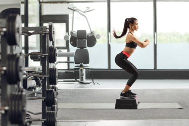 Genç bir kadının spor salonunda aerobik yaparken tam boy profil fotoğrafı.