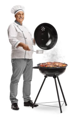 Şef, beyaz arka planda ızgarada et pişiriyor ve gülümsüyor.