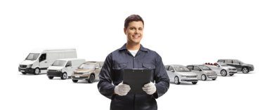 Mavi üniformalı bir otomobil tamircisi beyaz arka planda izole edilmiş araçların önünde bir pano tutuyor.